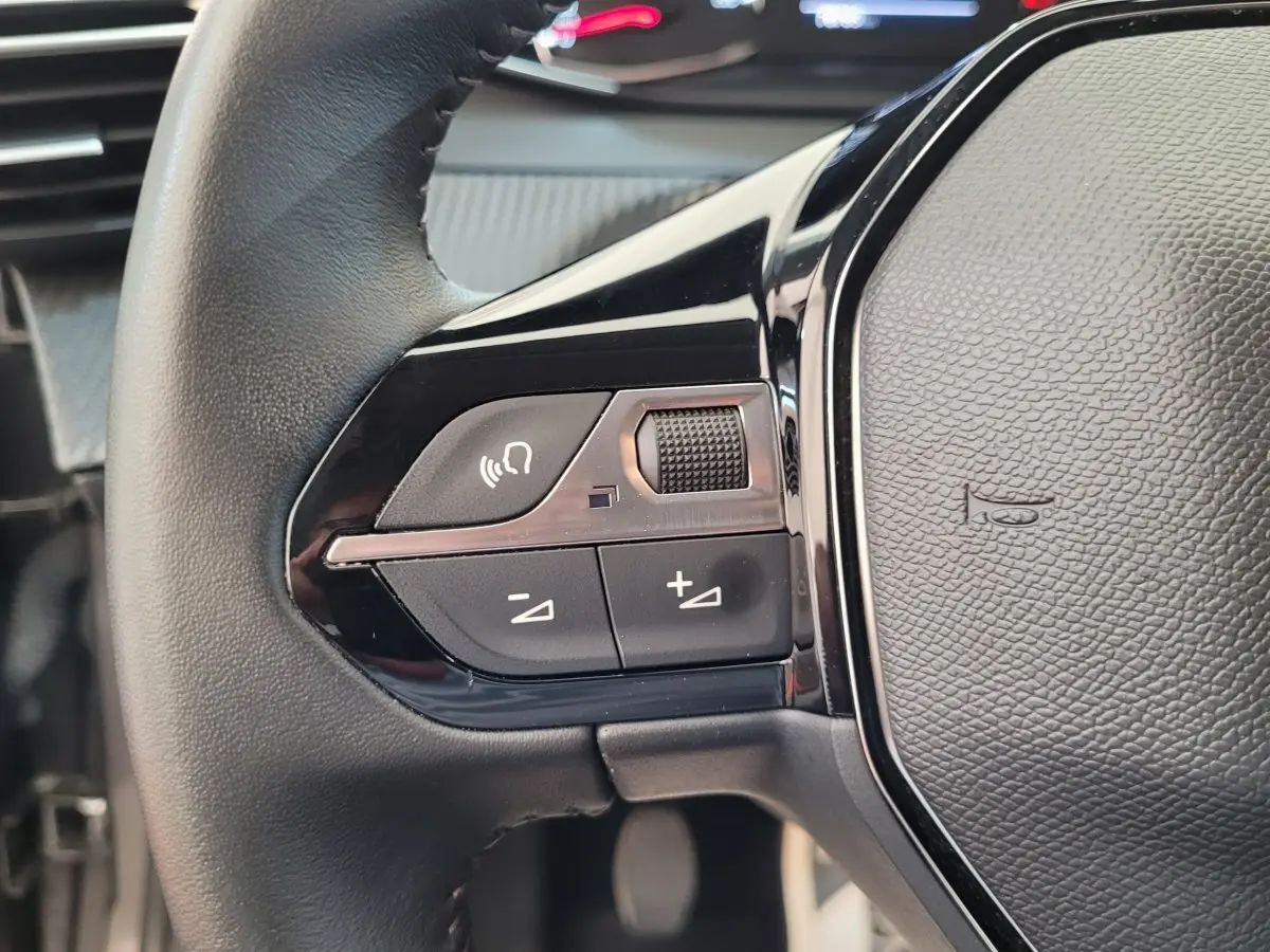 Gros plan sur la partie gauche du volant cuir de la Peugeot 208 gris foncé, avec commandes vocales et volume.