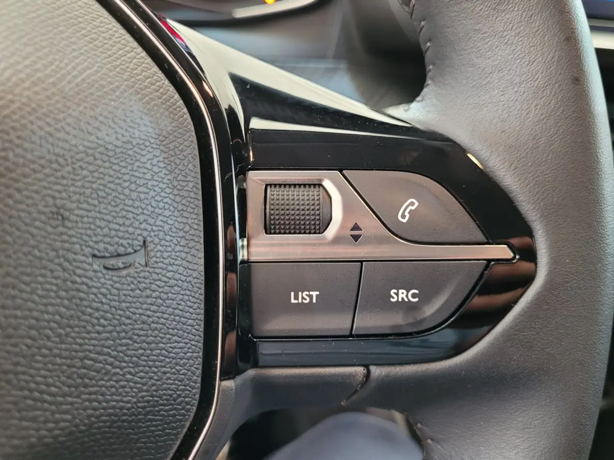 Gros plan sur les commandes gauche du volant cuir de la Peugeot 208 gris foncé, boutons LIST et SRC visibles.