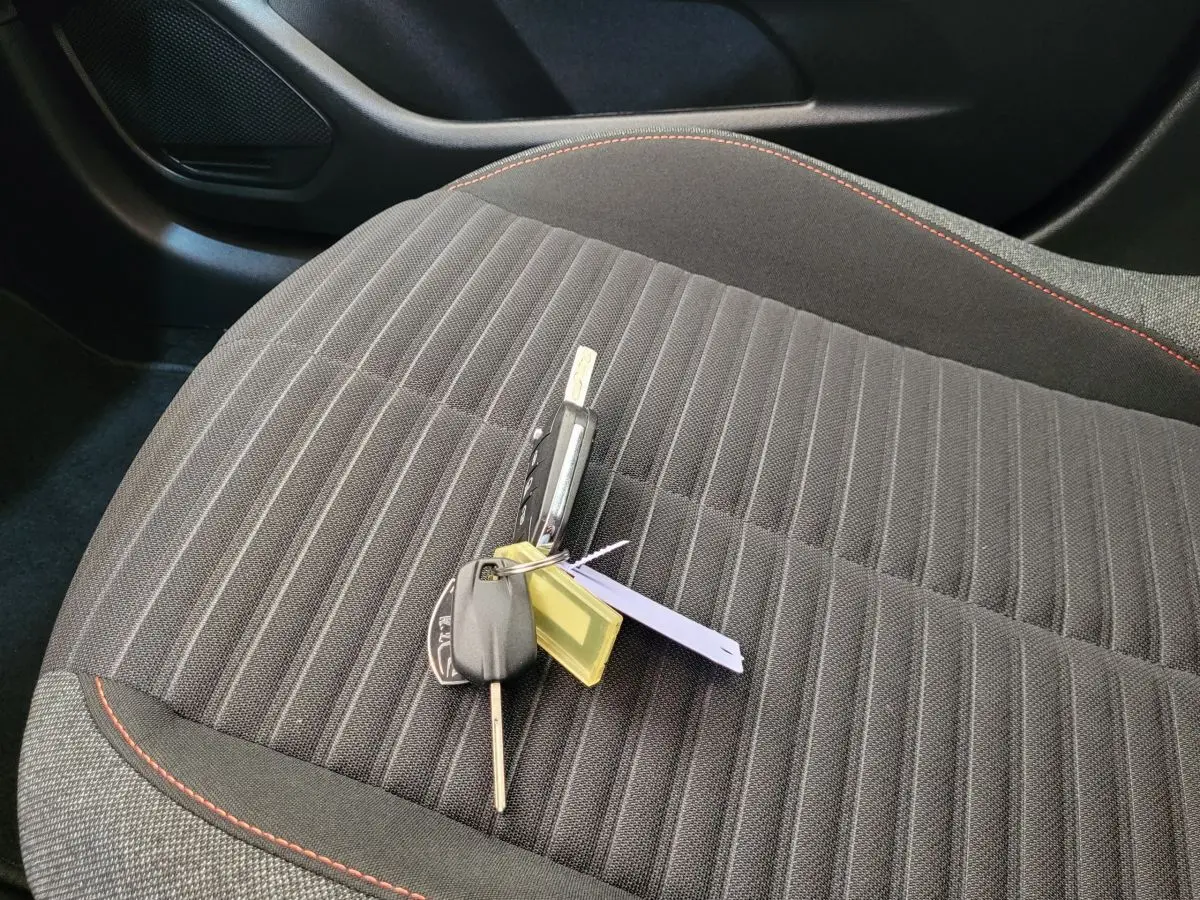 Clé de Peugeot 208 BlueHDi posée sur le siège avant tissu gris foncé avec surpiqûres rouges.