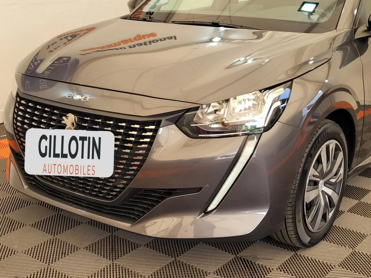 Vue 3/4 avant droit d'une Peugeot 208 gris foncé avec calandre distinctive et feux LED en forme de griffes.