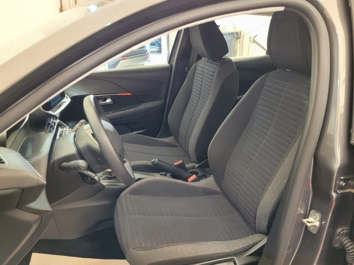 Intérieur vue côté conducteur de la Peugeot 208 gris foncé 2023, sièges tissu noir avec surpiqûres rouges.