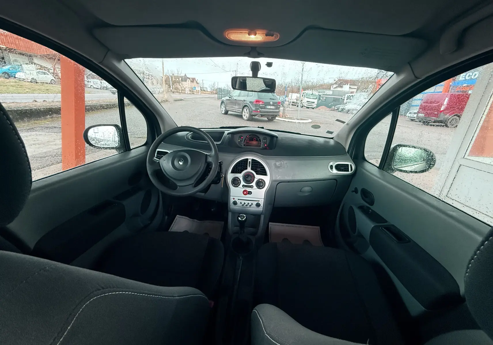 Vue intérieure avant du Renault Modus beige 2011, tableau de bord gris avec volant cuir et levier de vitesses manuel.