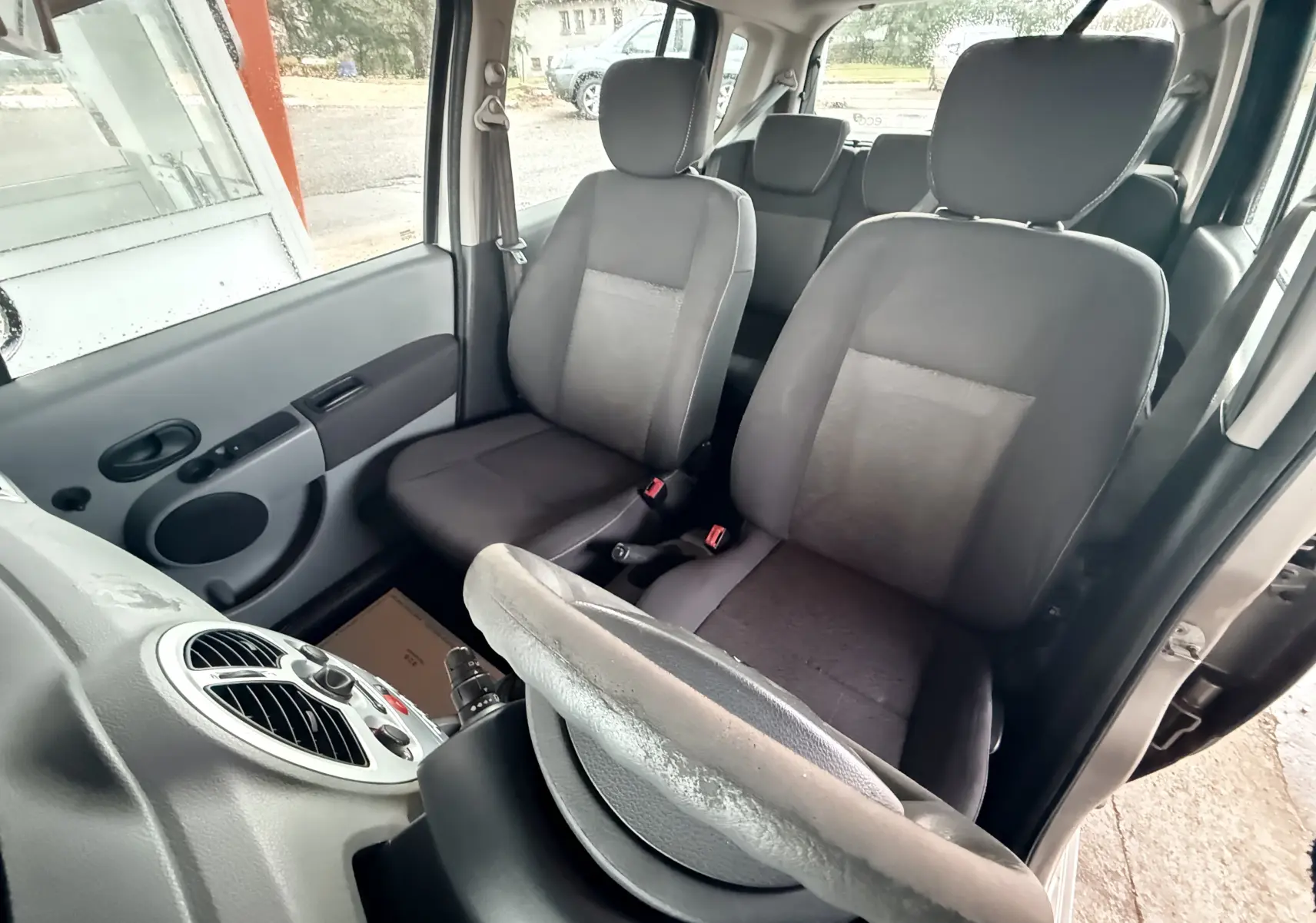 Vue intérieure côté conducteur de la Renault Modus beige, montrant les sièges avant gris et le volant en cuir.