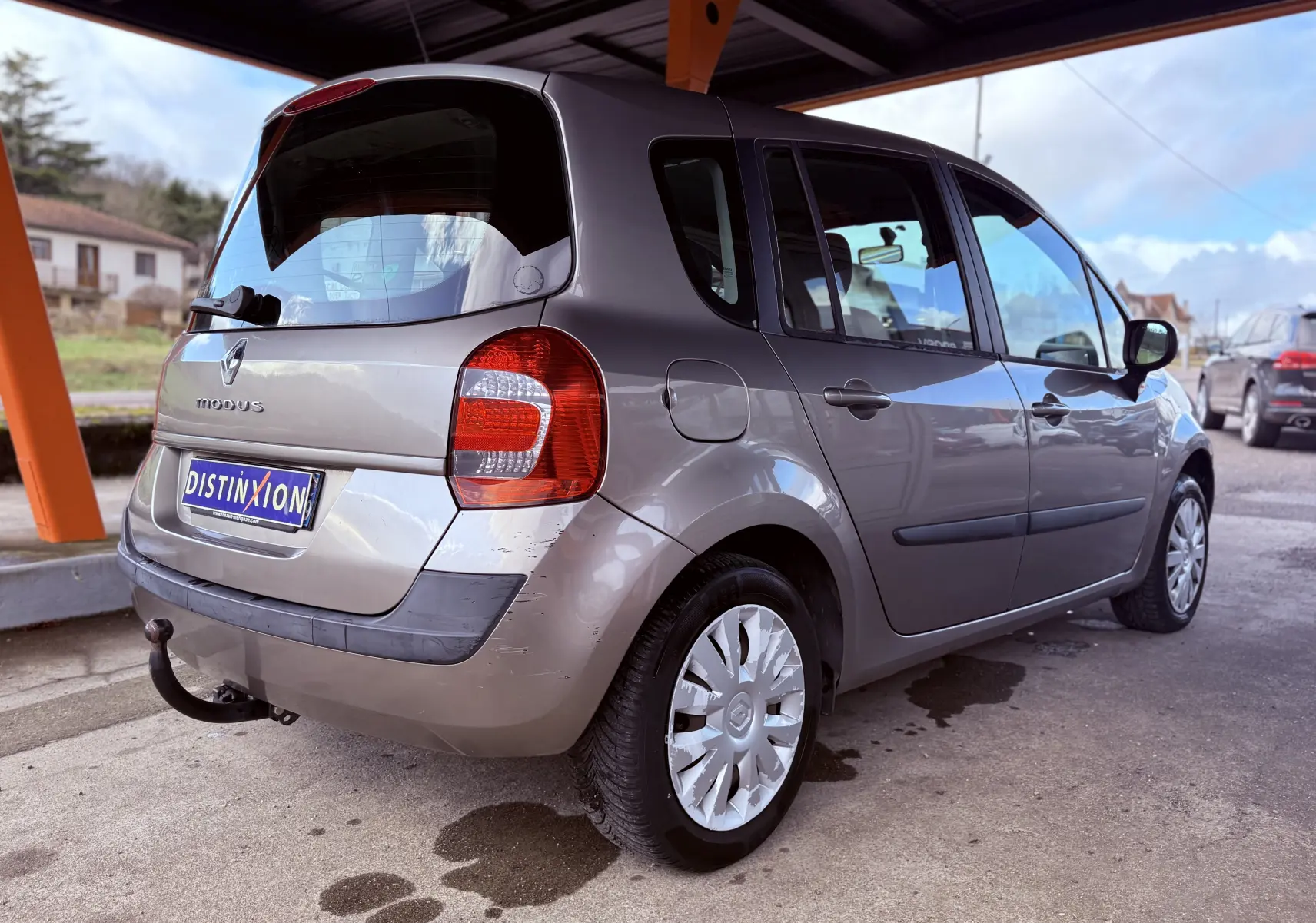 Vue 3/4 arrière droite d’une Renault Modus beige 5 portes avec attelage sous un abri.