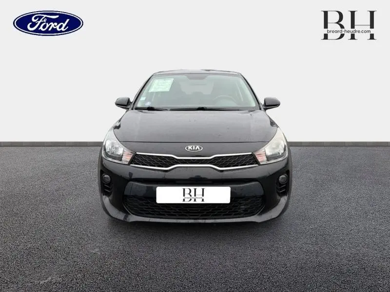 Vue avant d'une KIA Rio noire Ébène 2018 avec calandre chromée et phares halogènes allumés.