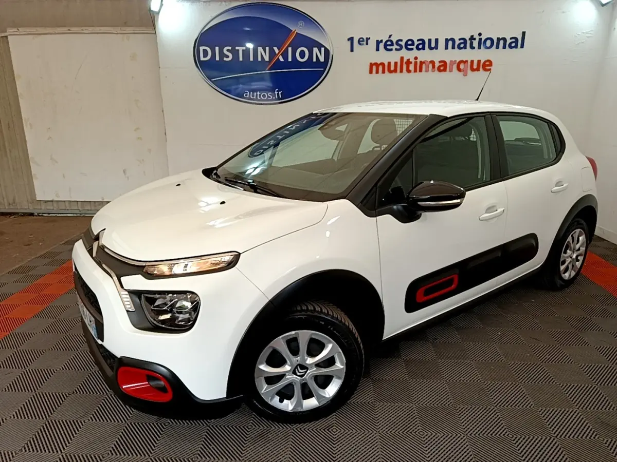 Citroën C3 blanche vue 3/4 avant droit, avec inserts rouges distinctifs sur les protections latérales et pare-chocs.