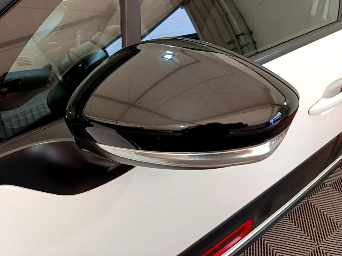 Gros plan sur le rétroviseur noir côté gauche d'une Citroën C3 blanche, avec partie de la portière visible.