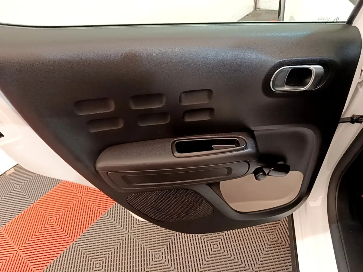 Vue rapprochée de la porte avant gauche noire et beige d'une Citroën C3 blanche, avec poignée et commande manuelle de vitre.