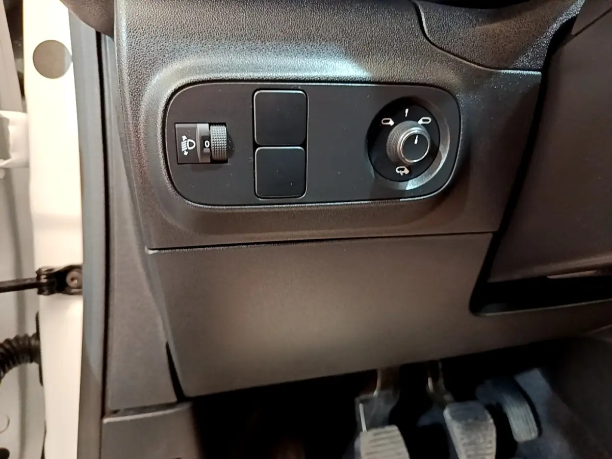 Détail intérieur côté gauche du tableau de bord noir de la Citroën C3 blanche, avec commandes des phares et rétroviseurs.