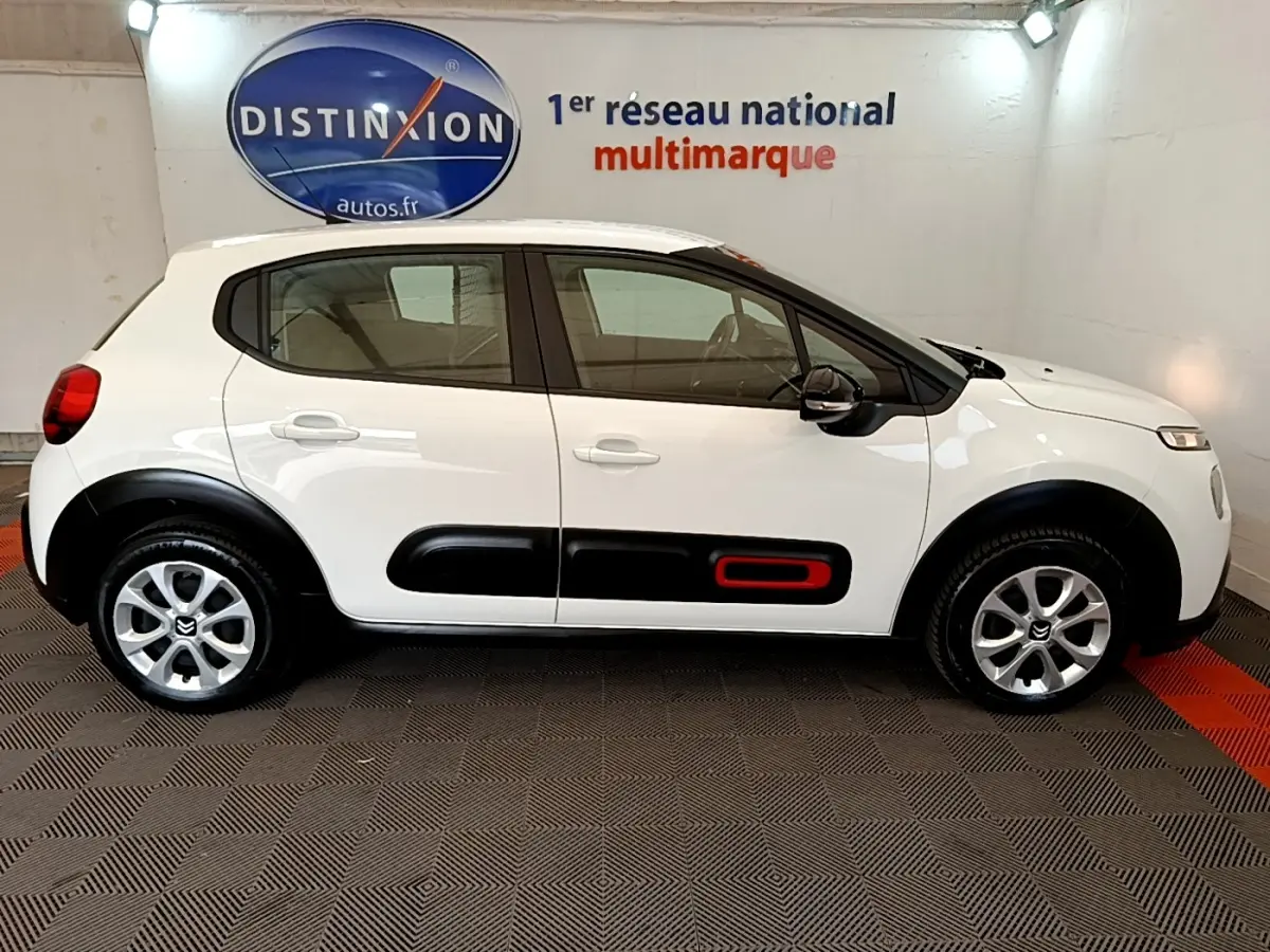 Profil droit d'une Citroën C3 blanche 2021 avec protections latérales noires et insert rouge, en intérieur showroom.