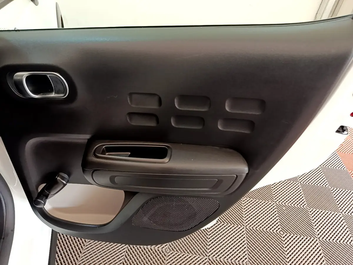 Vue rapprochée de la porte avant gauche noire avec poignée et manivelle sur une Citroën C3 blanche.