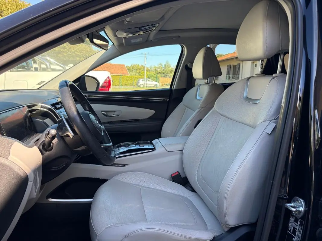 Vue intérieure côté conducteur du Hyundai Tucson noir 2022, sièges cuir gris clair et volant cuir avec console centrale.