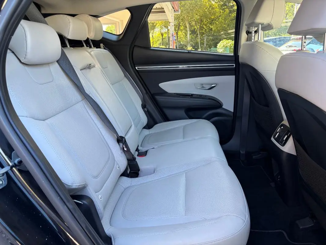 Vue intérieure arrière gauche du Hyundai Tucson 2022 noir, montrant la banquette claire en cuir et les détails de la porte.