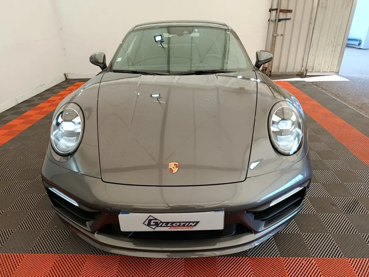 Vue avant d'une Porsche 911 Carrera 4S Coupé gris foncé, avec phares ronds LED et logo Porsche visible sur le capot.
