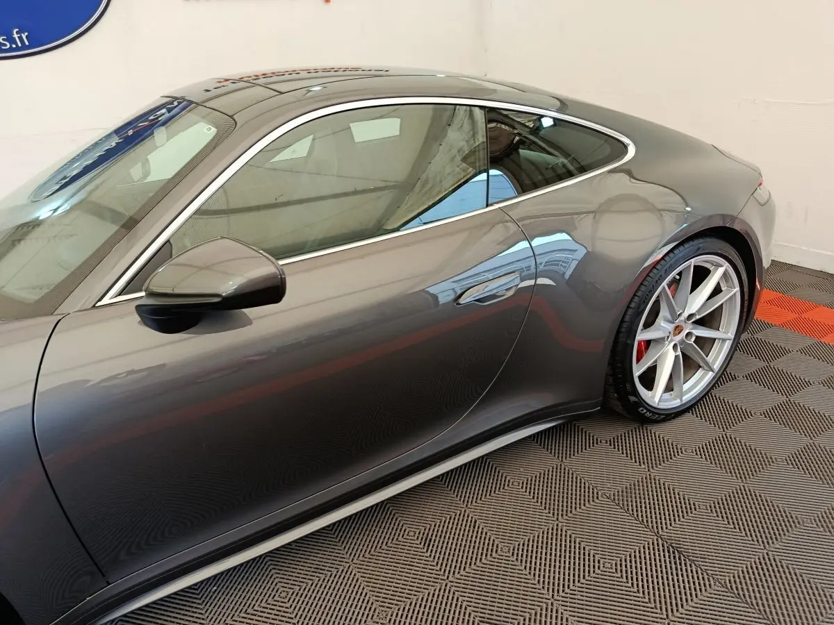 Profil côté gauche d'une Porsche 911 Carrera 4S Coupé gris foncé, mettant en valeur la jante alliage et la ligne fluide du toit.