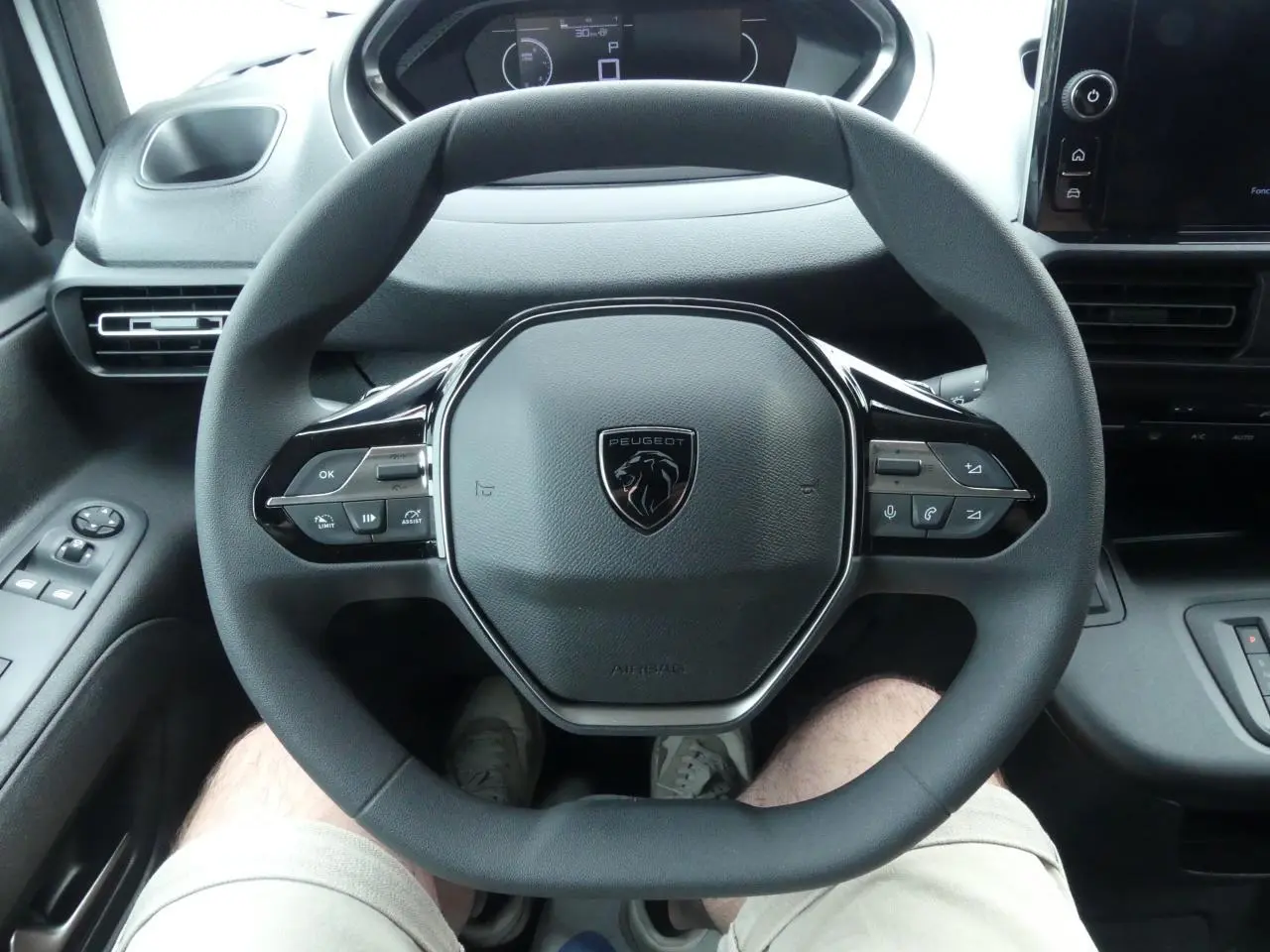 Vue rapprochée du volant multifonctions noir du Peugeot Partner 2025, avec tableau de bord et commandes visibles.