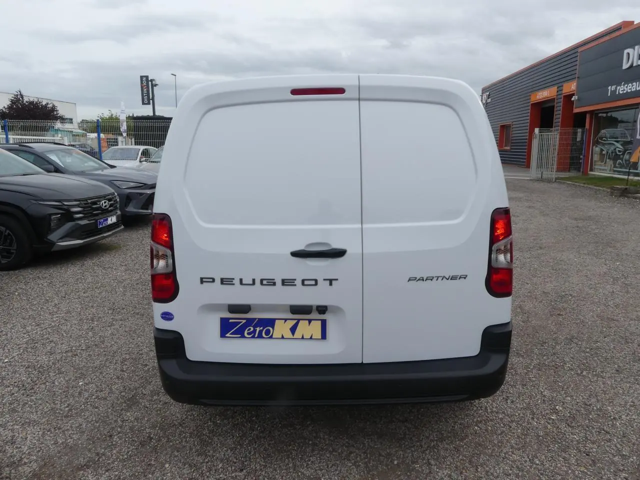 Vue arrière d'un utilitaire Peugeot Partner blanc avec portes battantes et logo visible sur un parking.
