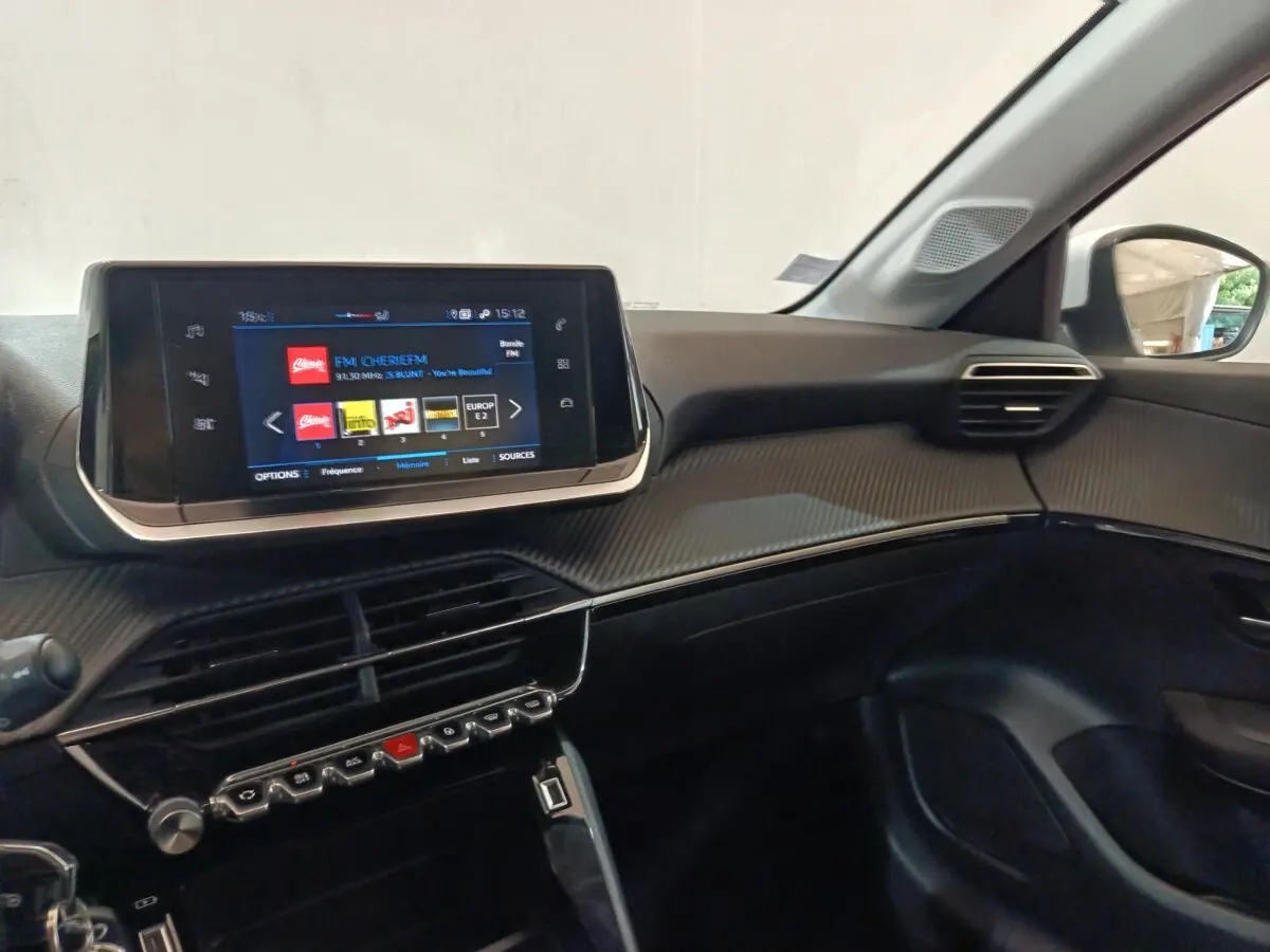 Vue intérieure côté passager du tableau de bord noir et écran tactile 7 pouces de la Peugeot 208 blanche PureTech 2020.