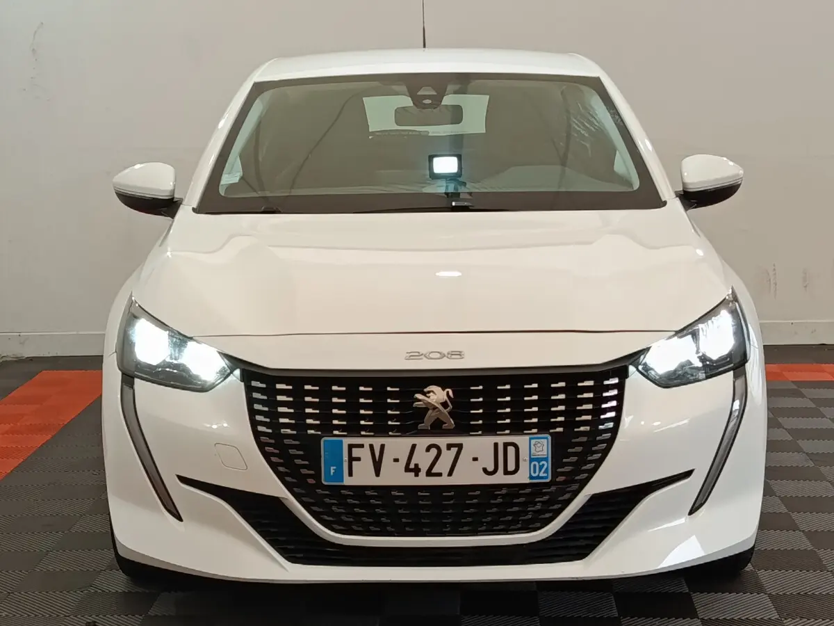Vue frontale d'une Peugeot 208 blanche de 2020 avec phares LED allumés et calandre noire distinctive.
