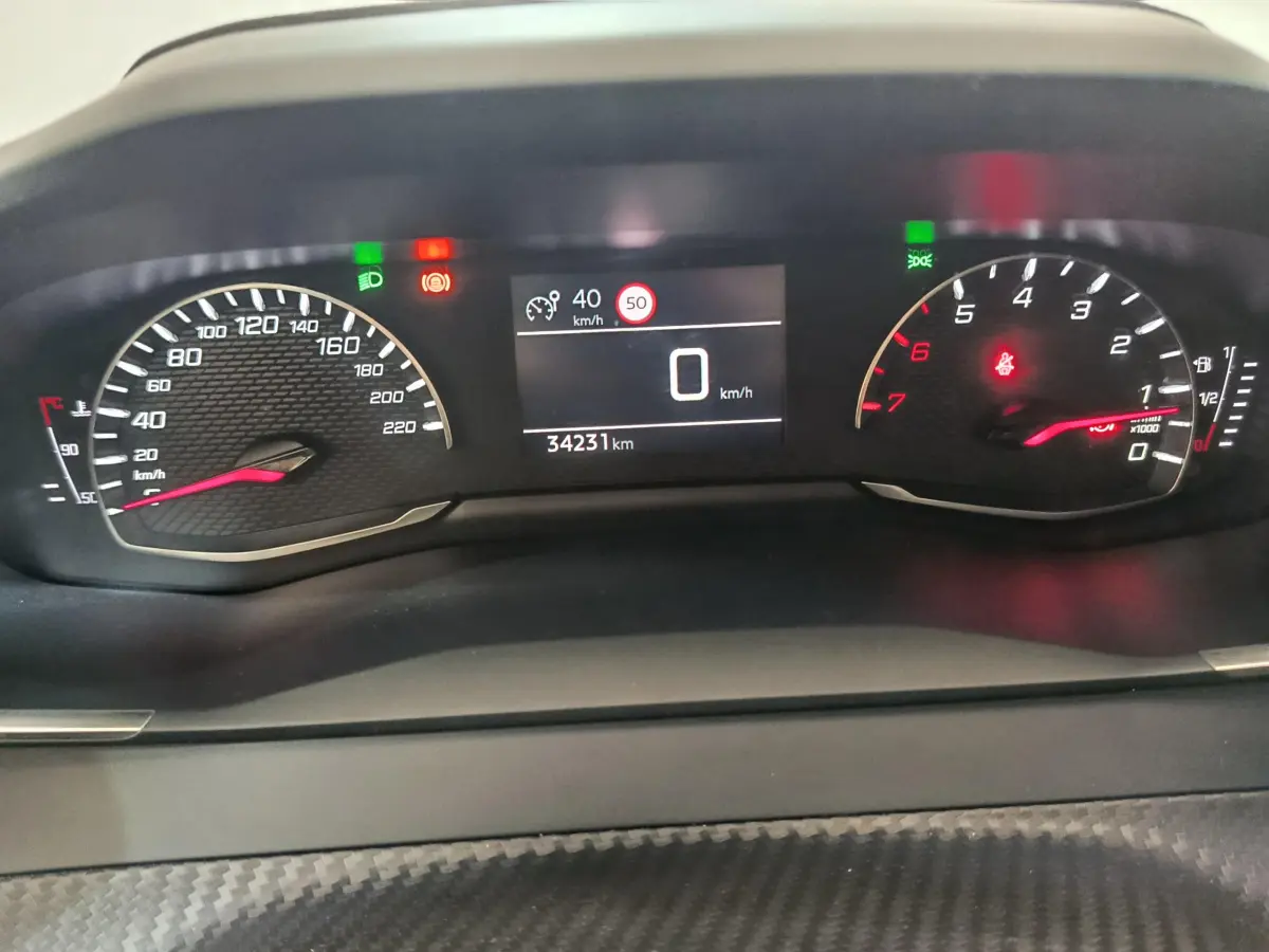 Vue rapprochée du tableau de bord numérique de la Peugeot 208 blanche, affichant vitesse et compte-tours.