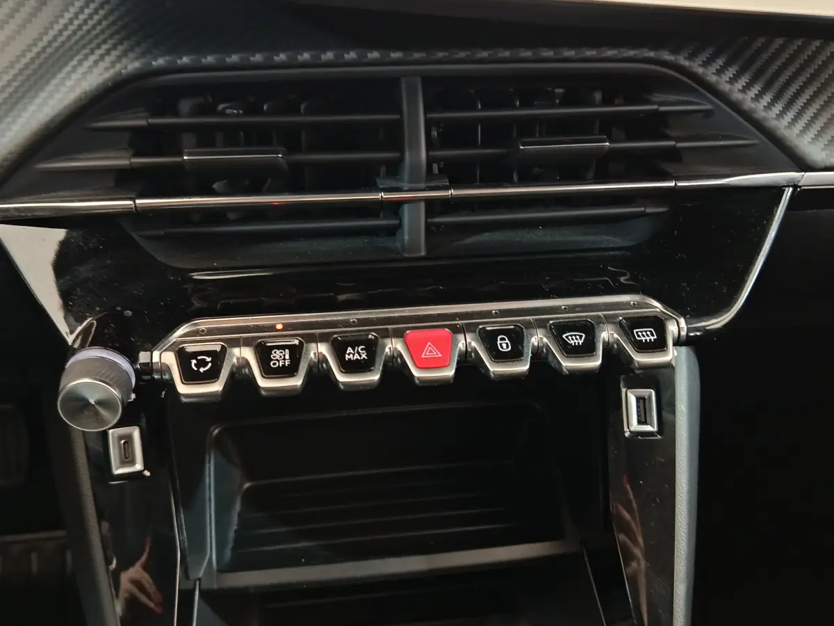 Vue rapprochée du tableau de bord noir de la Peugeot 208 blanche, avec boutons de commande et aérateurs visibles.