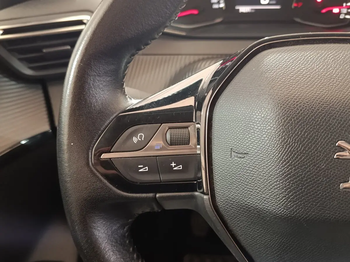 Gros plan sur le côté gauche du volant en cuir noir du Peugeot 208 blanc, avec commandes audio intégrées.