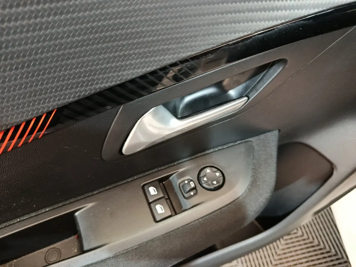 Gros plan sur la poignée intérieure et les commandes de vitres côté conducteur d'une Peugeot 208 blanche, finition Active Business.