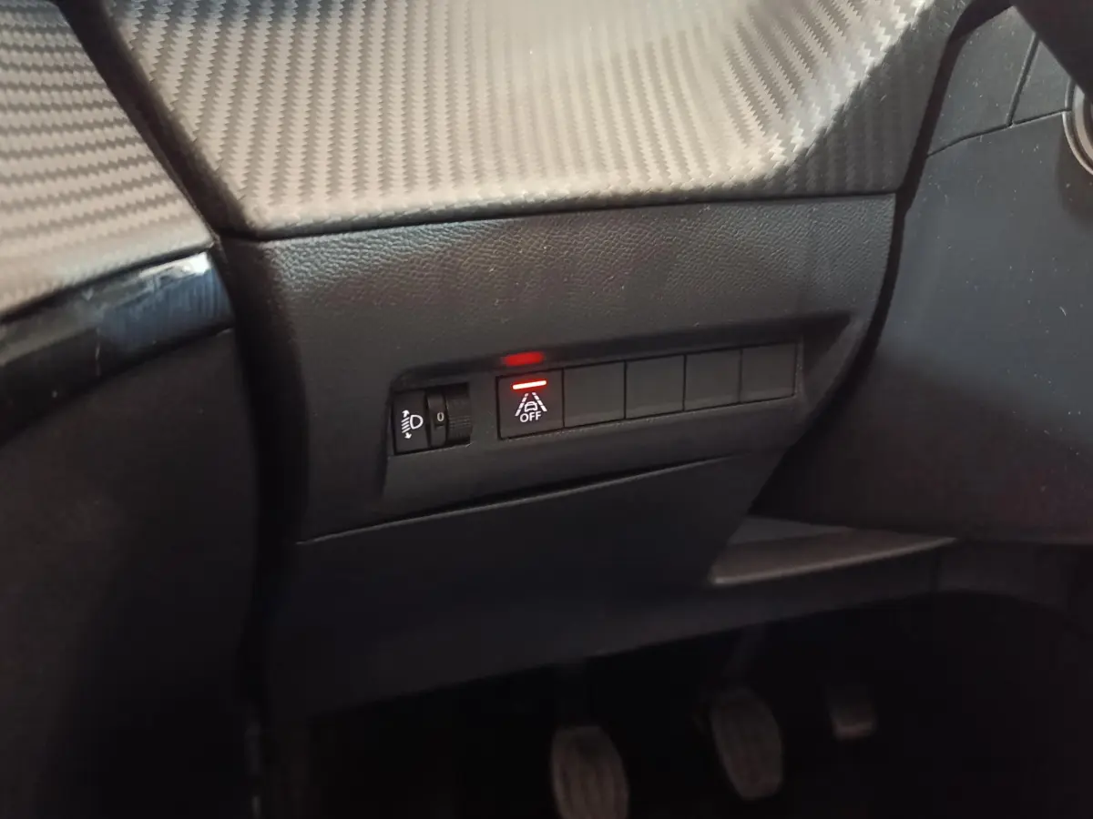 Détail du tableau de bord côté conducteur du Peugeot 208 blanc 2020 avec bouton d'assistance désactivée éclairé en rouge.
