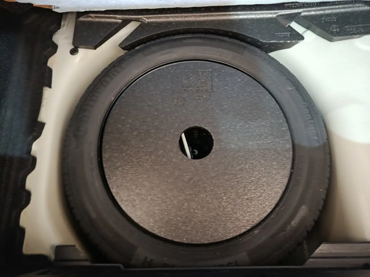 Vue plongeante sur la roue de secours noire dans le coffre blanc d'une Peugeot 208 PureTech 100 S&S Active Business 2020.