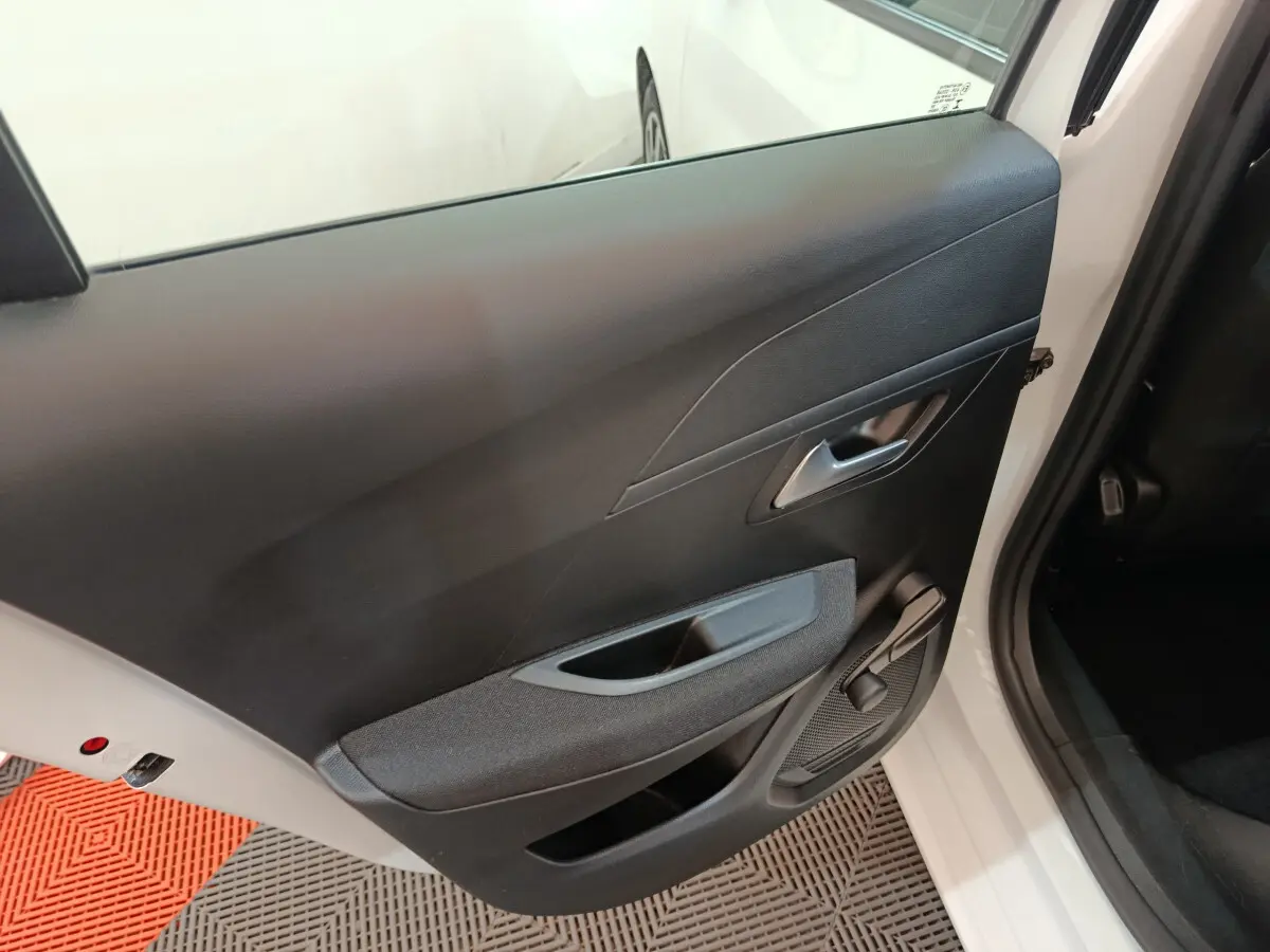 Vue intérieure de la porte arrière gauche noire d'une Peugeot 208 blanche, avec poignée et manivelle de vitre.
