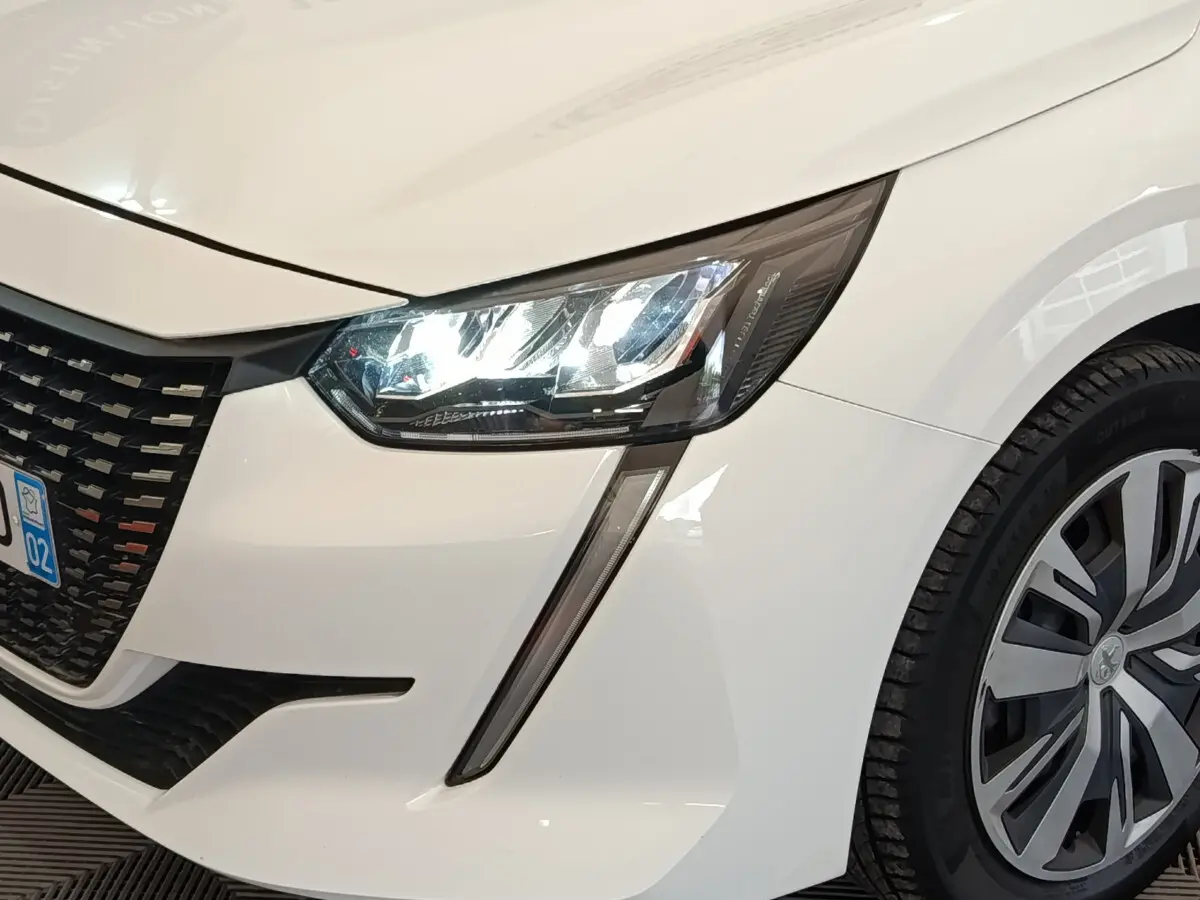 Gros plan sur l'avant droit d'une Peugeot 208 blanche, mettant en valeur son phare LED et la calandre noire.