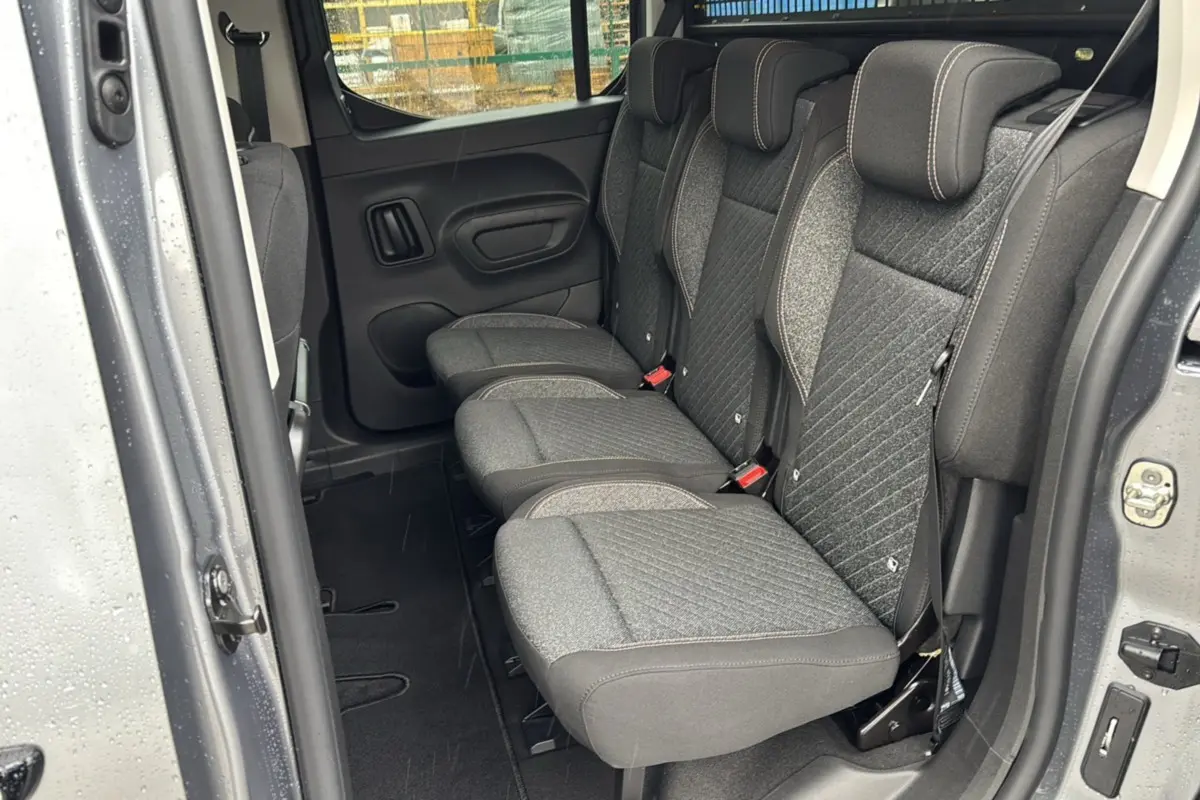 Vue latérale intérieure sur les sièges arrière tissu gris du Peugeot Rifter 2025 gris artense avec porte coulissante ouverte.