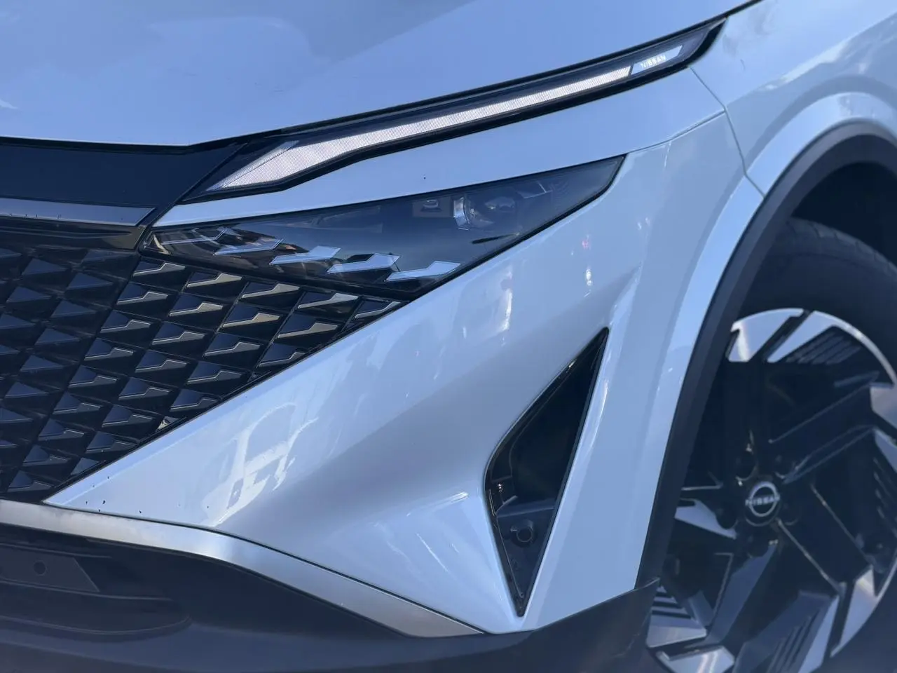Gros plan sur l'avant droit du Nissan Qashqai blanc nacré, mettant en valeur le phare LED et la calandre noire.
