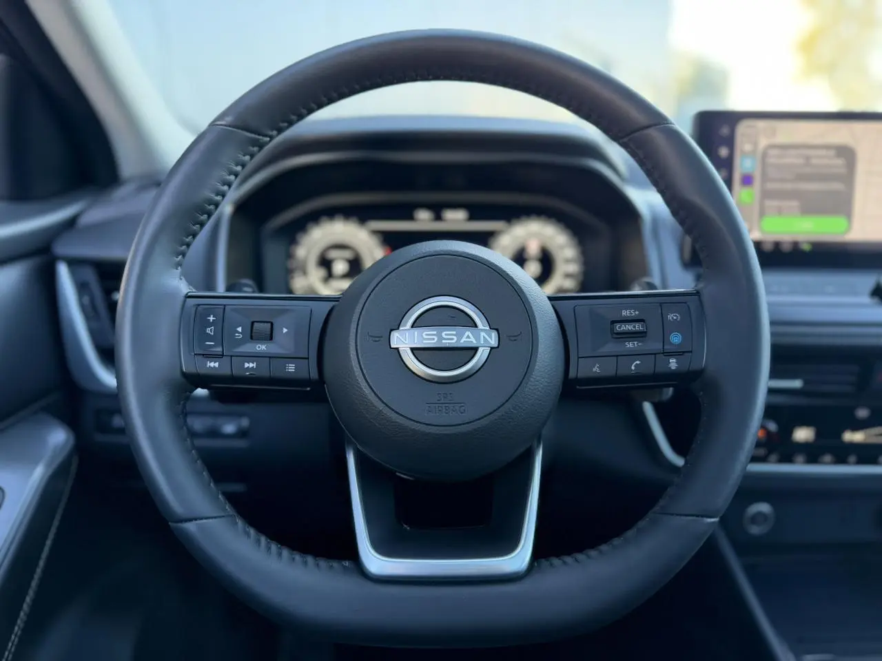 Vue frontale du volant cuir noir du Nissan Qashqai 2025 avec commandes intégrées et tableau de bord numérique flou.
