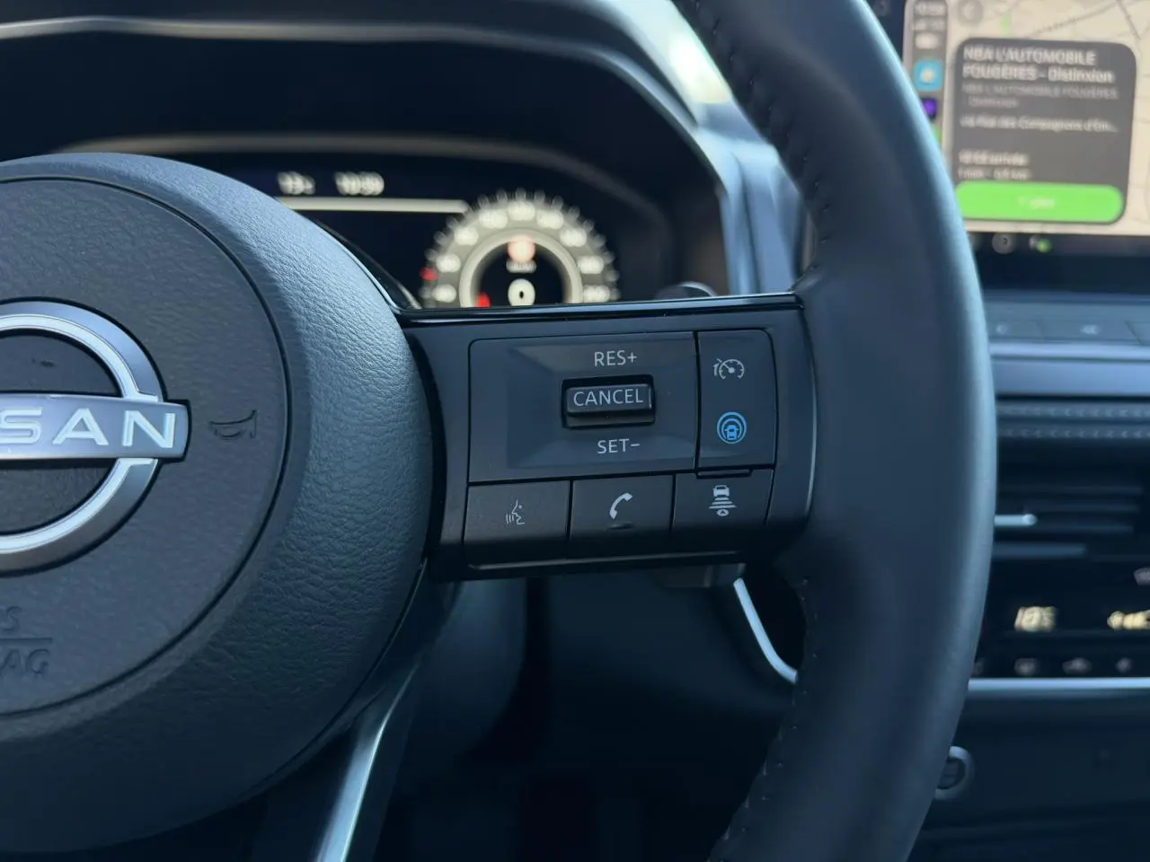 Gros plan sur le volant noir cuir du Nissan Qashqai 2025, avec commandes intégrées et tableau de bord numérique flou en arrière-plan.