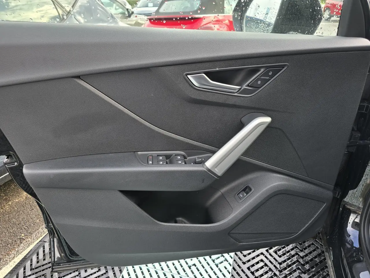 Vue rapprochée de la porte avant gauche noire mythic de l'Audi Q2 35 TFSI avec commandes de vitres et poignée argentée.