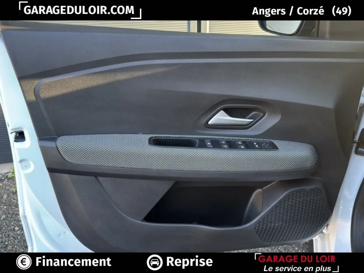 Intérieur de la porte avant gauche d'une Dacia Sandero blanche 2025, avec habillage tissu gris et commandes électriques.