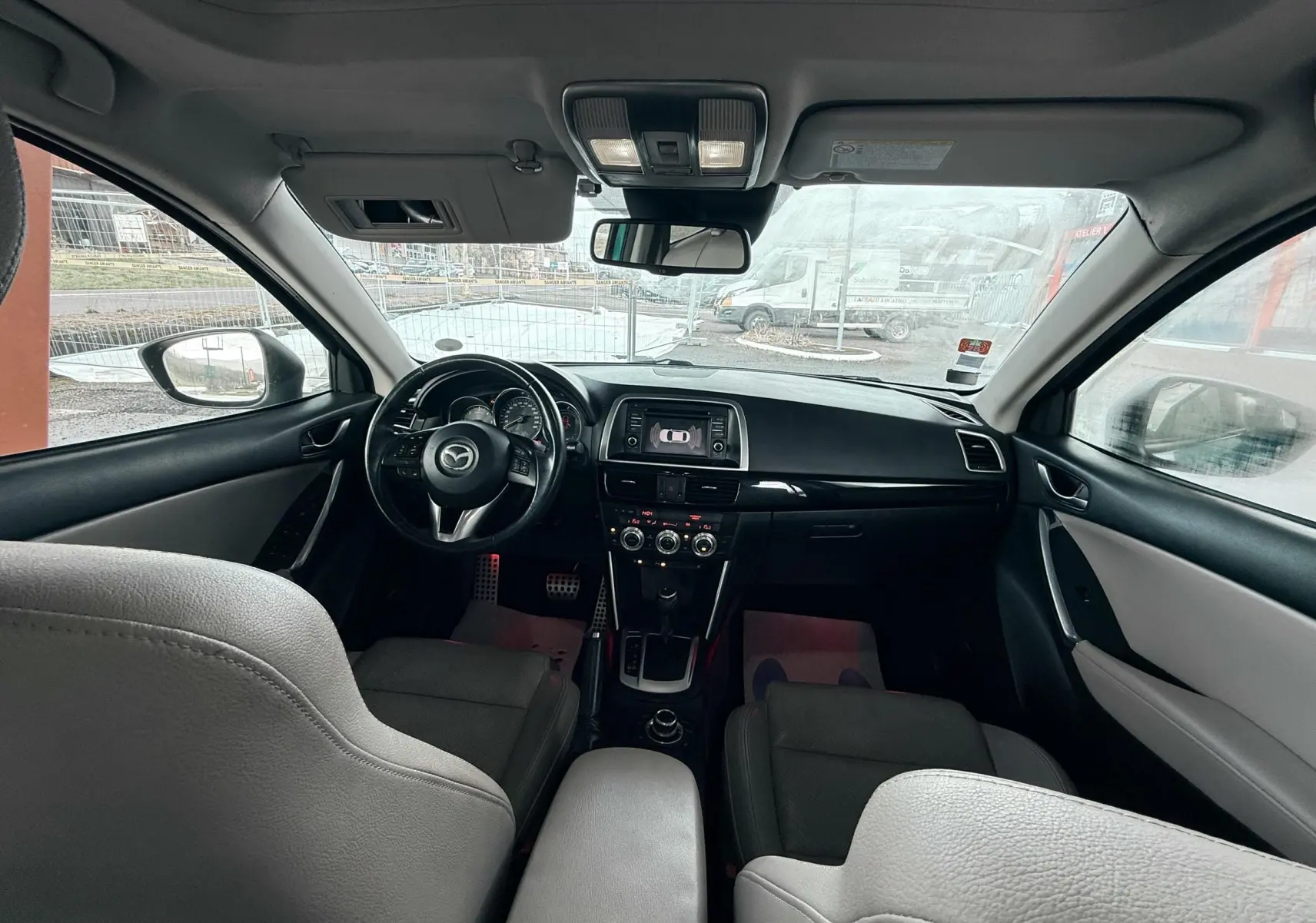 Vue intérieure avant du Mazda CX-5 2013, tableau de bord noir avec écran central et volant multifonction.