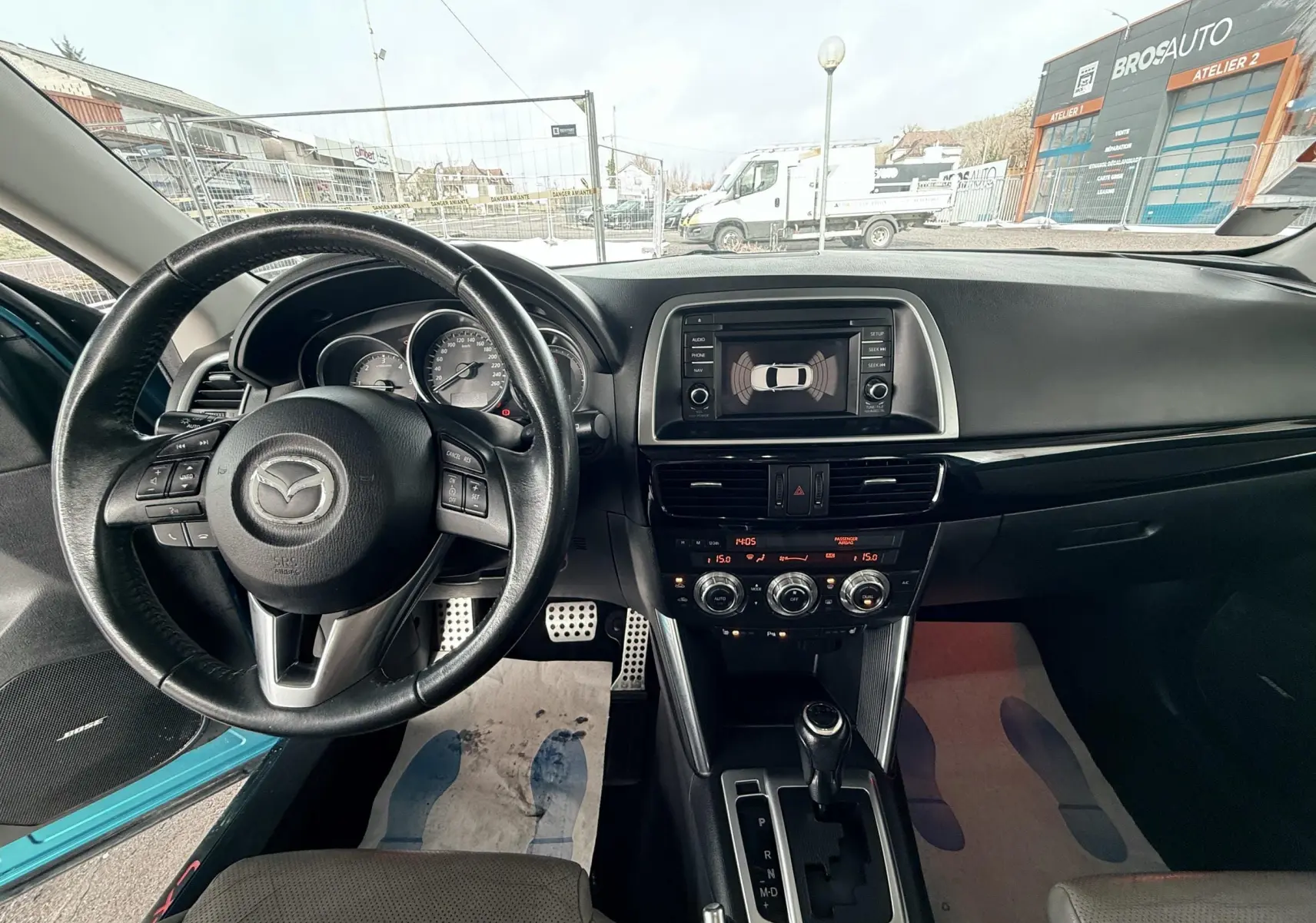 Vue intérieure du tableau de bord et volant du Mazda CX-5 bleu 2013, avec écran central et commande de boîte automatique.