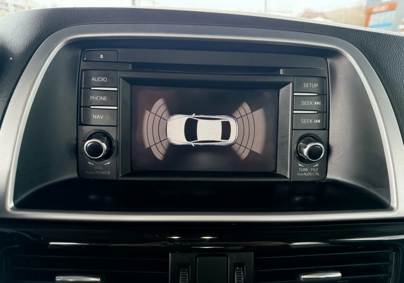 Écran central du Mazda CX-5 2013 montrant l'affichage du système d'aide au stationnement avec boutons de commande autour.