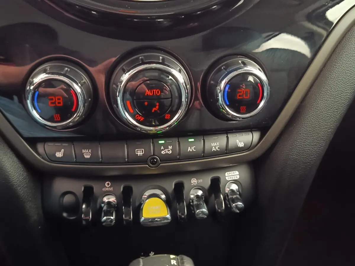 Gros plan sur la console centrale du MINI Countryman noir, montrant les commandes de climatisation et le bouton start/stop jaune.