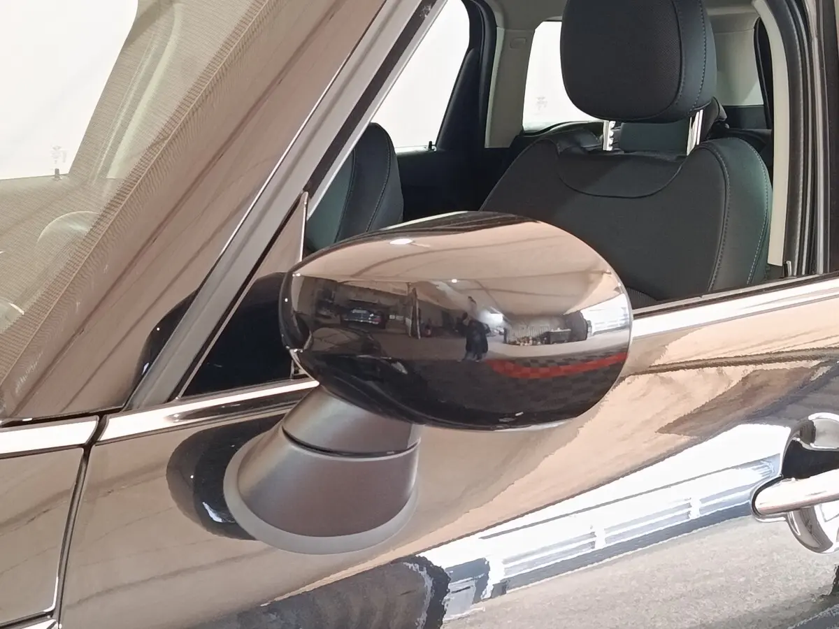 Gros plan sur le rétroviseur côté gauche noir brillant du MINI Countryman Cooper SE 2023 avec intérieur en cuir noir visible.