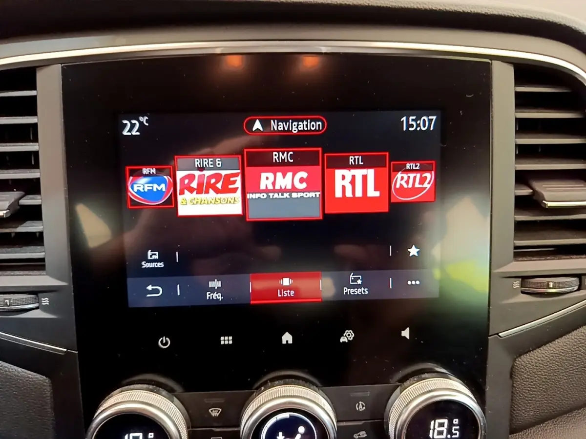 Écran tactile central affichant la navigation et stations radio dans l’habitacle d’une Renault Mégane Business E-Tech hybride blanche.