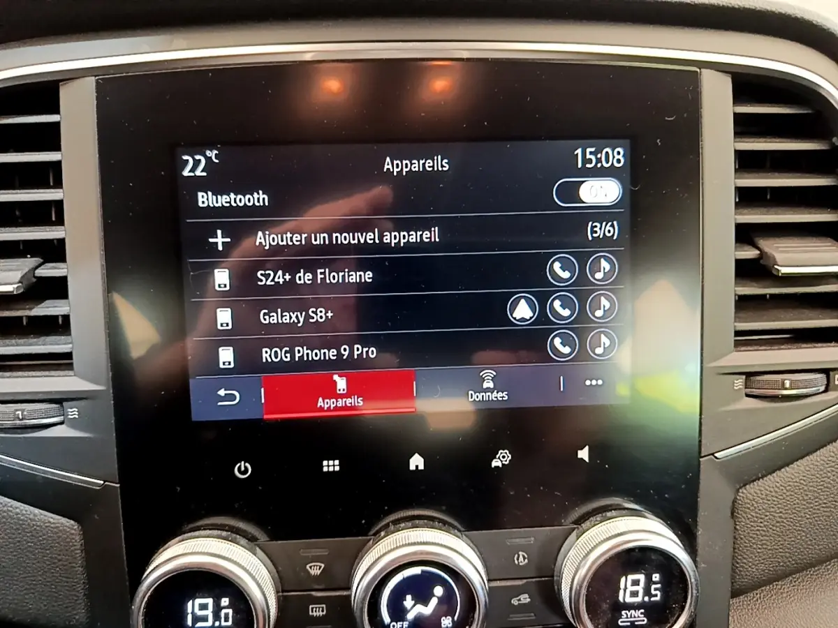 Écran tactile central de la Renault Mégane Business E-Tech hybride blanc, affichage Bluetooth et commandes climatisation visibles.