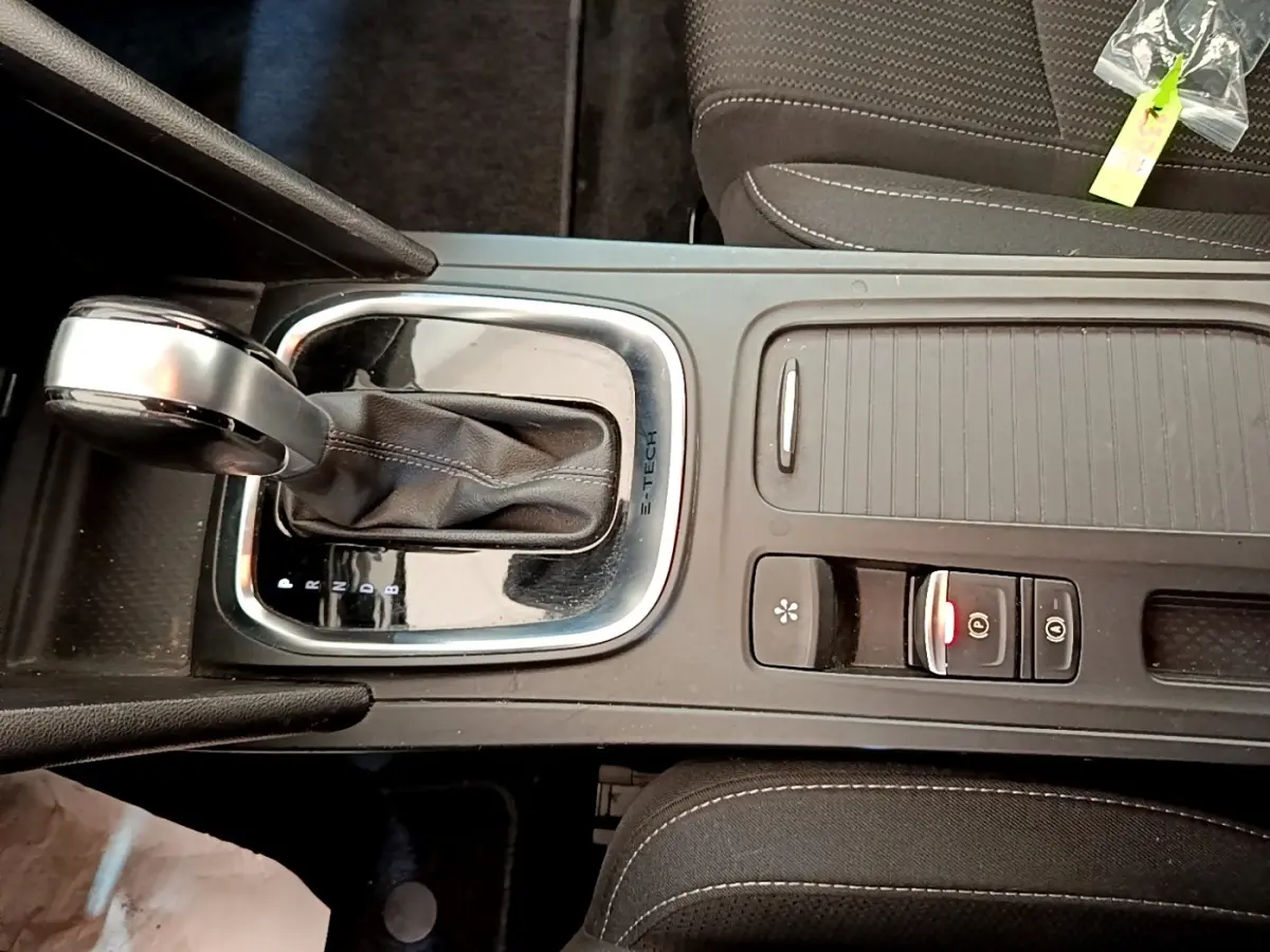 Gros plan sur la console centrale noire de la Renault Mégane Business E-Tech hybride, avec levier de vitesse automatique et commandes.