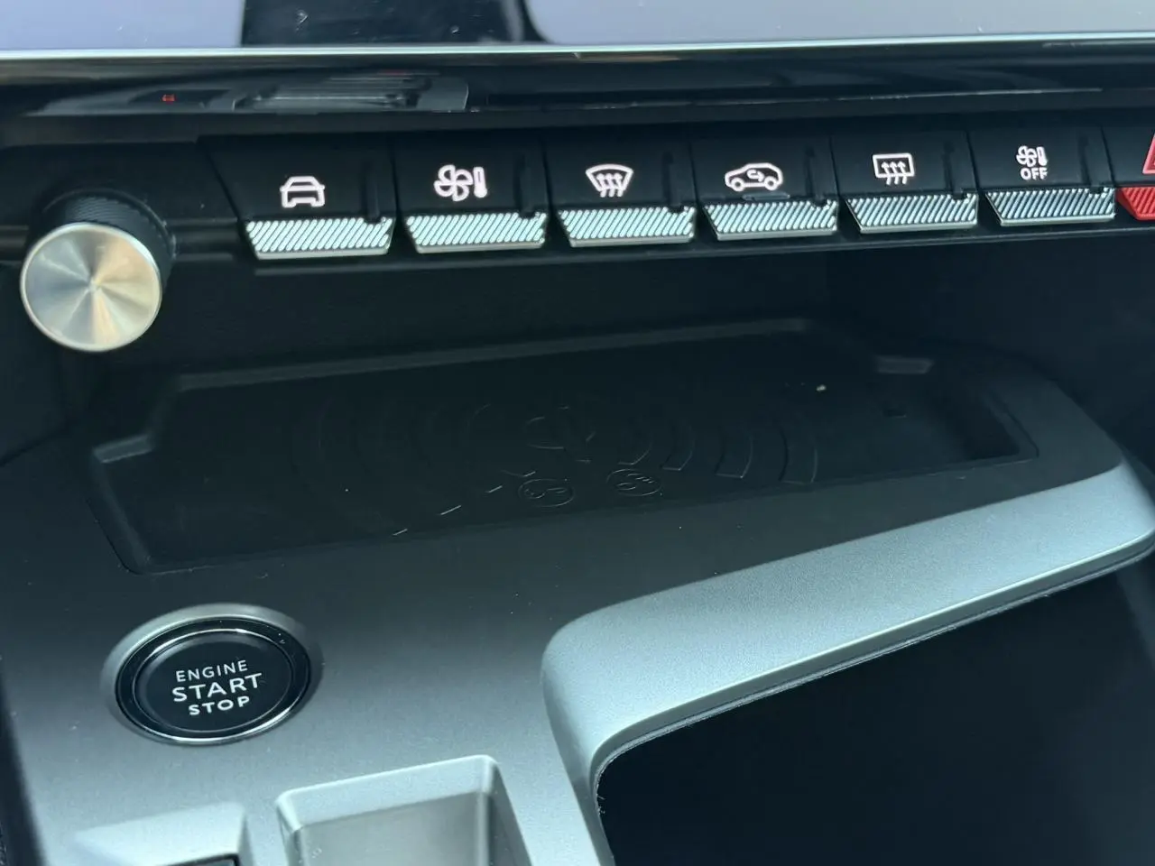 Détail intérieur du Peugeot 308 Hybrid 2025 montrant la zone de charge sans fil et le bouton start/stop, finition noire.