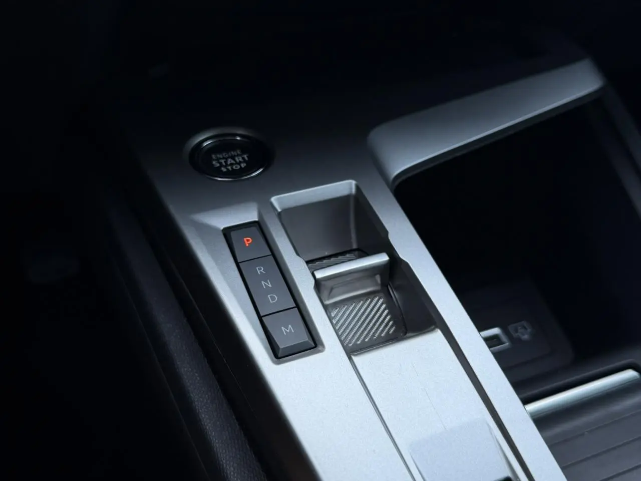 Gros plan sur la console centrale argentée de la Peugeot 308 Hybrid 2025 avec boutons de boîte auto et bouton start/stop.
