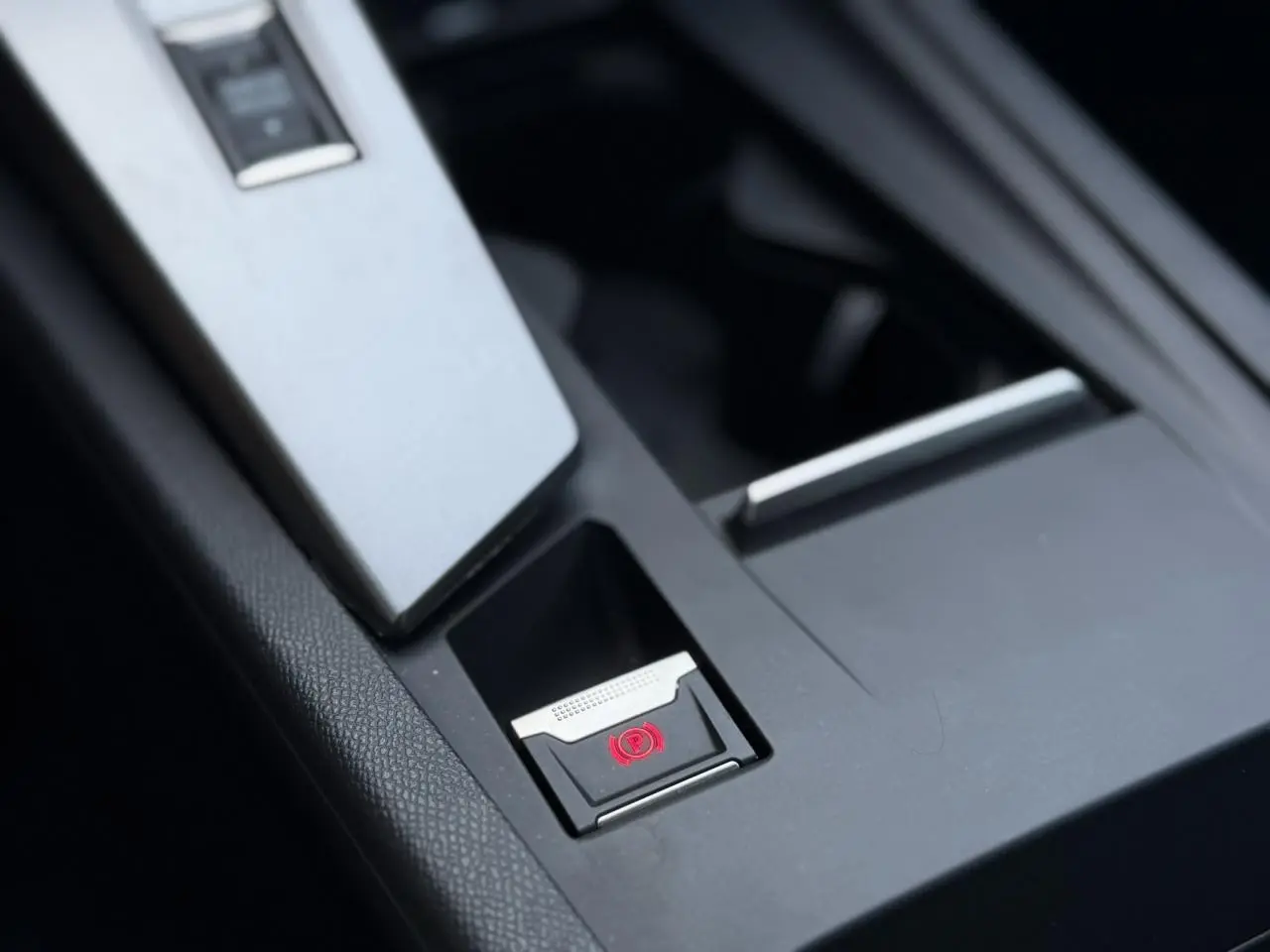 Gros plan sur la console centrale noire de la Peugeot 308 Hybrid avec bouton de frein de parking électronique éclairé en rouge.