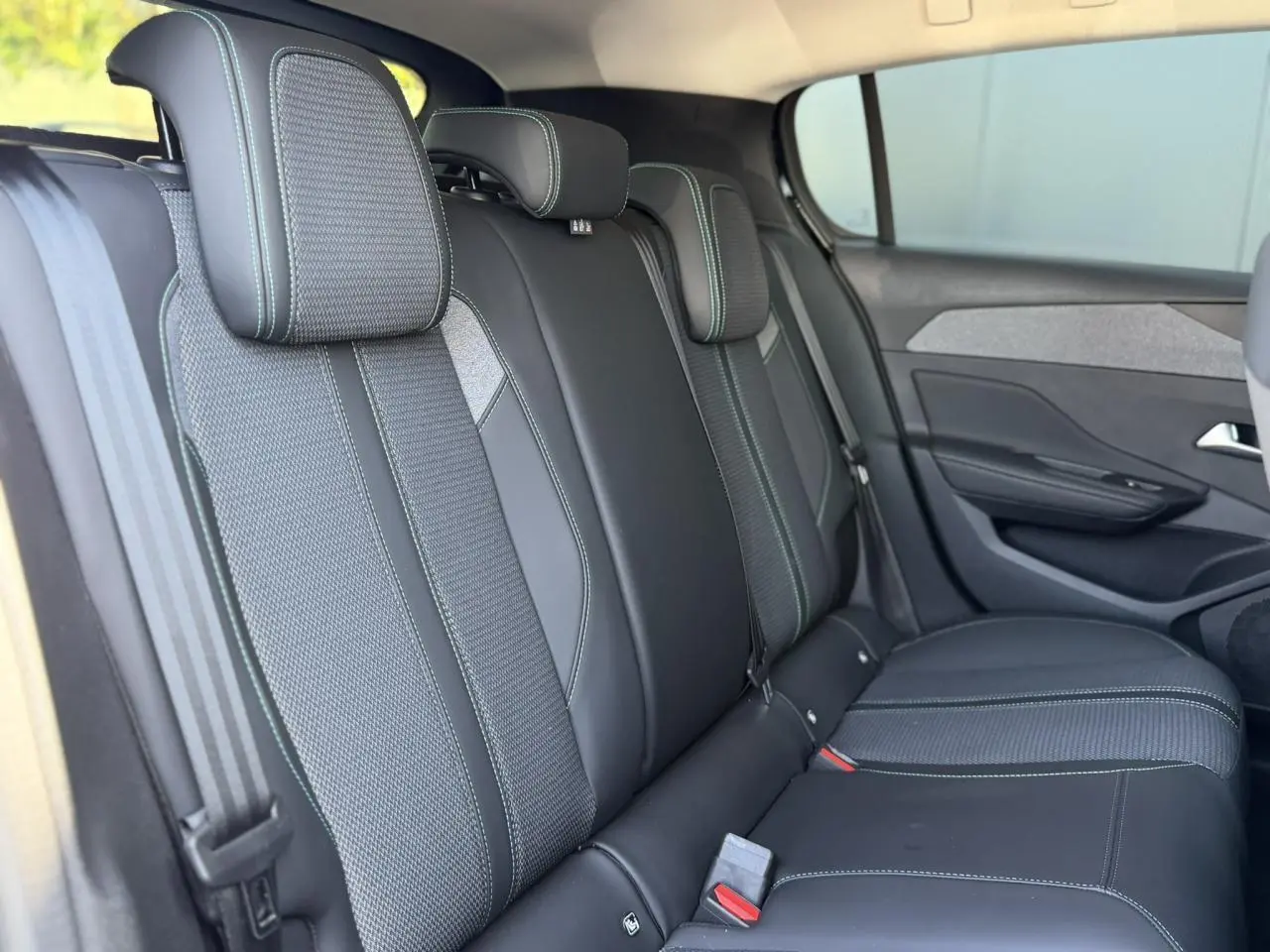 Vue latérale des sièges arrière noirs avec surpiqûres bleues de la Peugeot 308 Hybrid 2025, finition Allure.