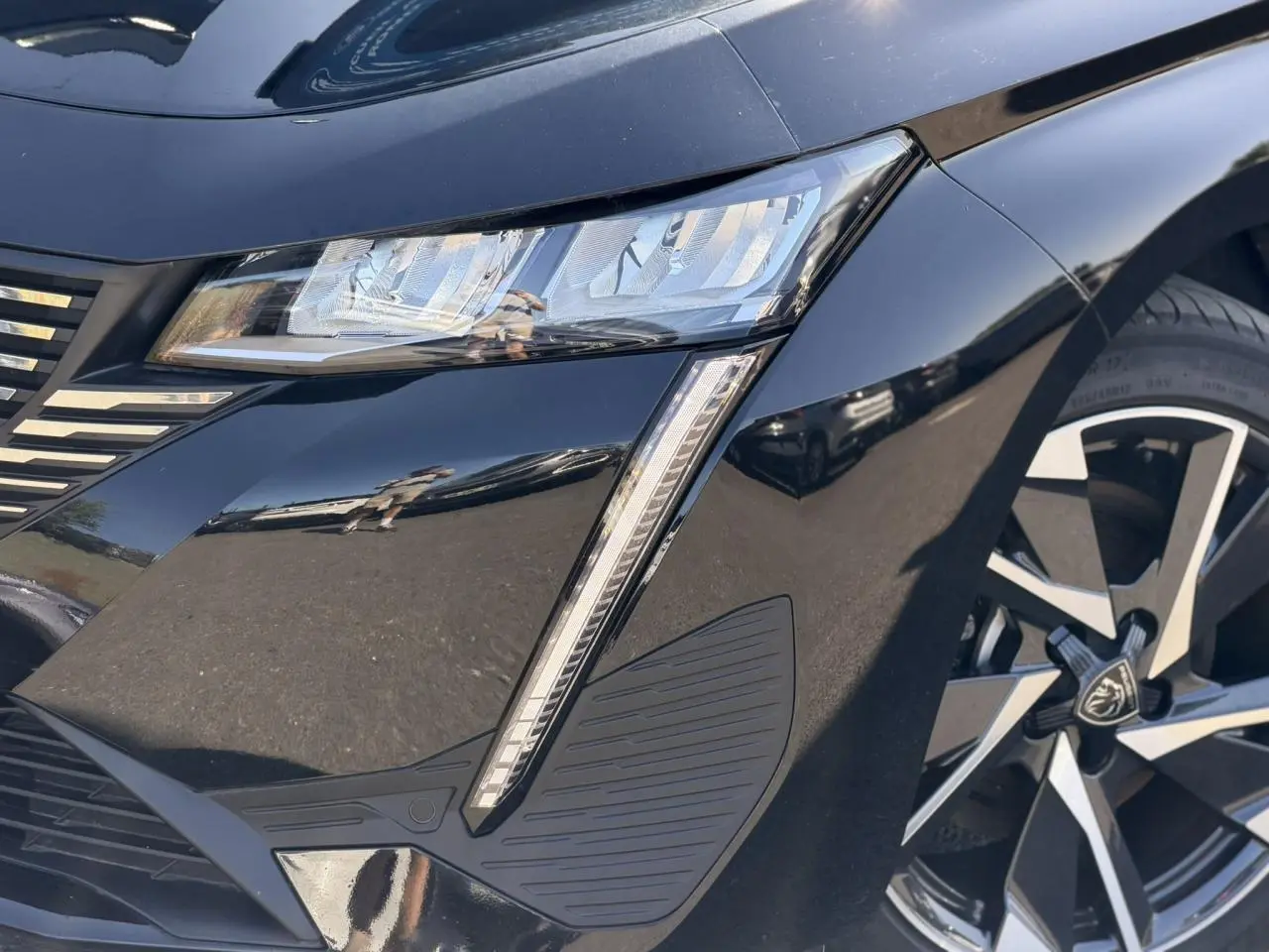 Gros plan sur l'avant droit noir Perla de la Peugeot 308 Hybrid 2025, mettant en valeur le phare LED et la jante alliage 17'' Halong.